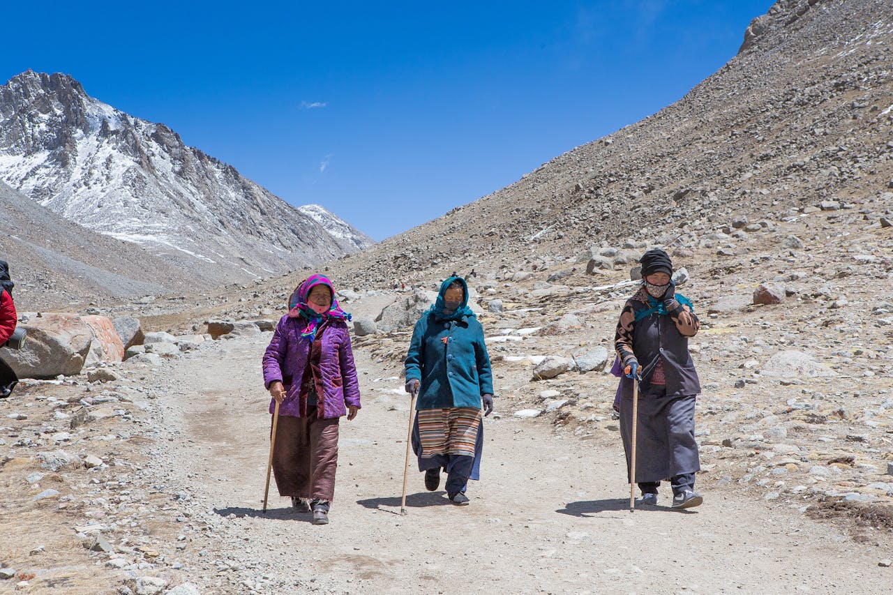 Three women trek through Ngari's mountainous terrain, clad in traditional attire and using walking sticks.